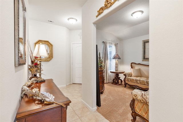 hallway with visible vents, light carpet, vaulted ceiling, light tile patterned flooring, and baseboards