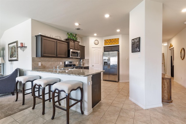 kitchen featuring light stone counters, a sink, dark brown cabinets, appliances with stainless steel finishes, and backsplash