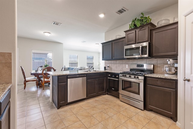 kitchen featuring light stone counters, visible vents, dark brown cabinets, appliances with stainless steel finishes, and tasteful backsplash