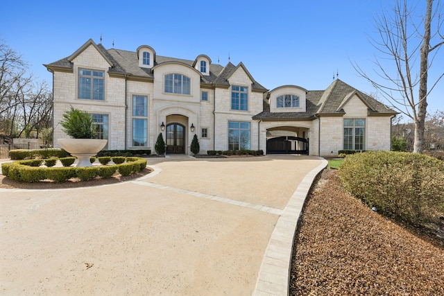 french country style house featuring stone siding, concrete driveway, fence, and french doors