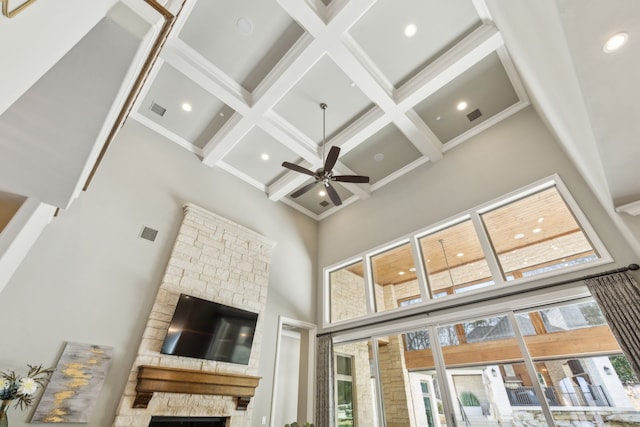 living area with a towering ceiling, visible vents, coffered ceiling, and a stone fireplace