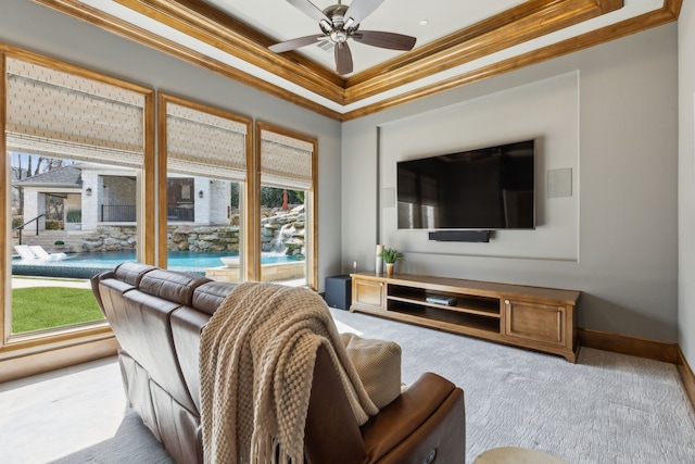 living area with ceiling fan, carpet floors, baseboards, a raised ceiling, and crown molding