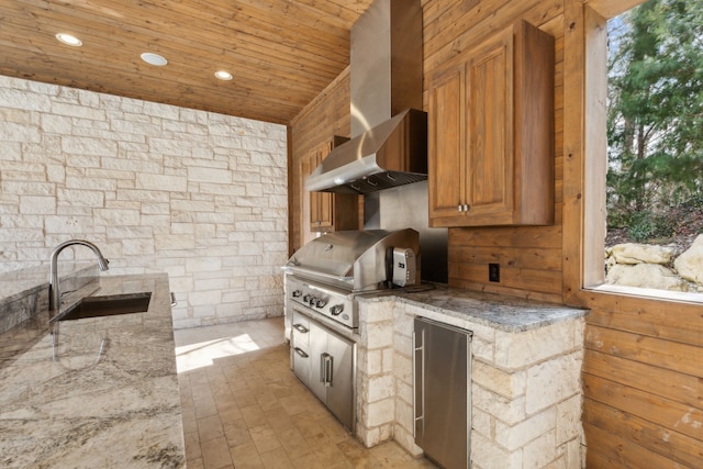 kitchen with light stone counters, a sink, wooden ceiling, wall chimney exhaust hood, and stainless steel refrigerator