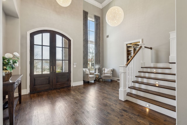 entryway featuring arched walkways, french doors, a wealth of natural light, a towering ceiling, and wood finished floors