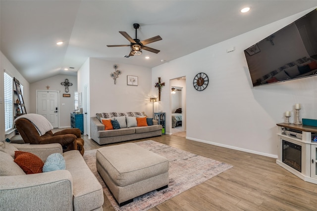 living area featuring light wood-type flooring, a wealth of natural light, a glass covered fireplace, and lofted ceiling