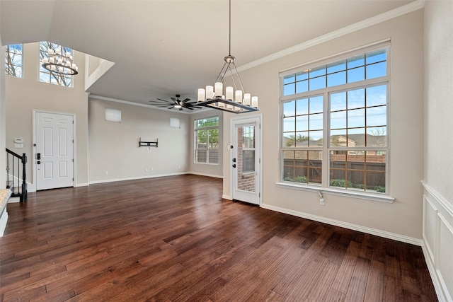 unfurnished dining area with dark wood-style floors, ornamental molding, ceiling fan with notable chandelier, and baseboards