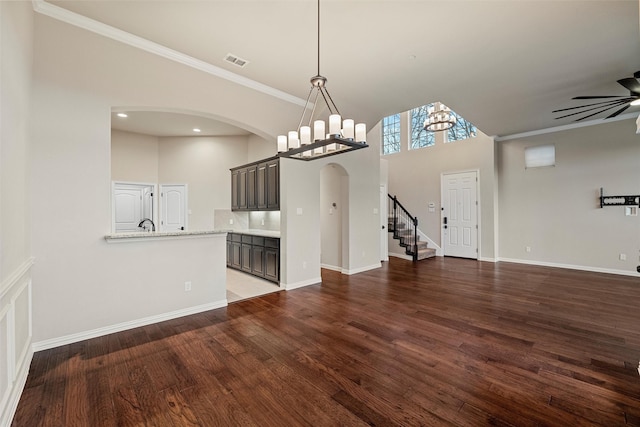 unfurnished living room with dark wood-style floors, arched walkways, visible vents, baseboards, and ceiling fan with notable chandelier