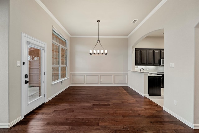 unfurnished dining area with dark wood-type flooring, a chandelier, a wainscoted wall, and ornamental molding