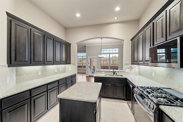 kitchen featuring arched walkways, a kitchen island, stainless steel appliances, a sink, and recessed lighting