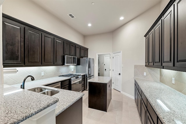 kitchen featuring light stone counters, stainless steel appliances, visible vents, a sink, and a kitchen island