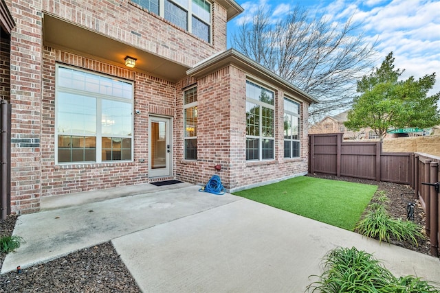 property entrance with a patio area, fence, and brick siding