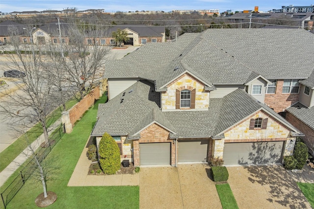 view of front of home featuring a shingled roof, fence, a garage, stone siding, and driveway