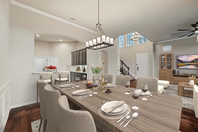 dining space featuring arched walkways, dark wood-style flooring, crown molding, and ceiling fan with notable chandelier