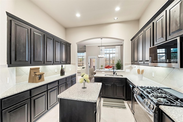 kitchen featuring arched walkways, a kitchen island, stainless steel microwave, a sink, and gas stove