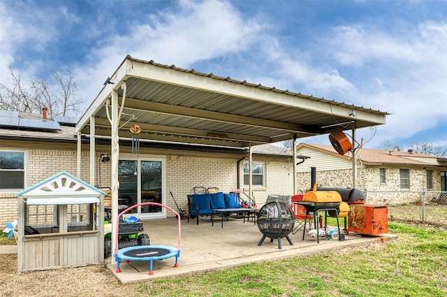 rear view of house with an outdoor living space with a fire pit, fence, a patio area, roof mounted solar panels, and brick siding