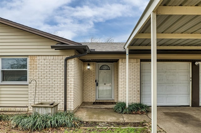 doorway to property featuring a garage, concrete driveway, brick siding, and roof with shingles