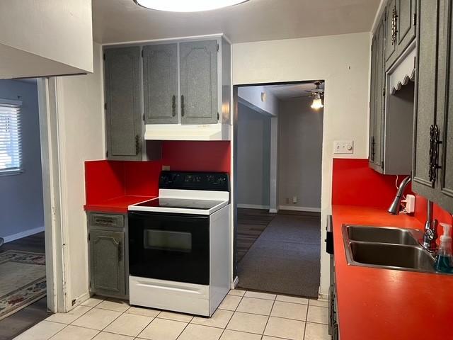 kitchen with light tile patterned floors, range with electric cooktop, decorative backsplash, under cabinet range hood, and a sink