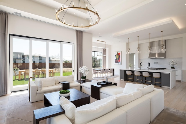 living room with light wood-style floors, a raised ceiling, indoor wet bar, and a notable chandelier