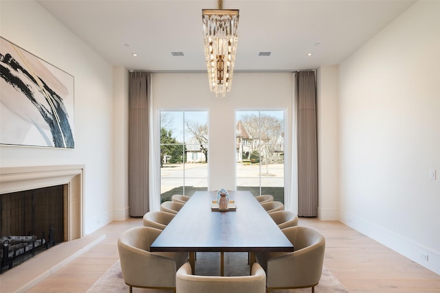 dining room featuring a notable chandelier, light wood finished floors, recessed lighting, a fireplace with raised hearth, and baseboards