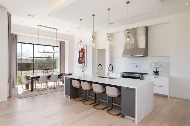 kitchen featuring stainless steel gas stove, wall chimney exhaust hood, modern cabinets, light countertops, and a sink