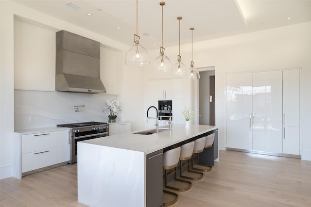 kitchen with a sink, light countertops, wall chimney range hood, stainless steel gas stove, and modern cabinets