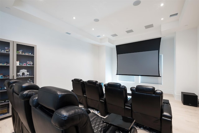 home theater room featuring light wood-type flooring, a raised ceiling, and visible vents