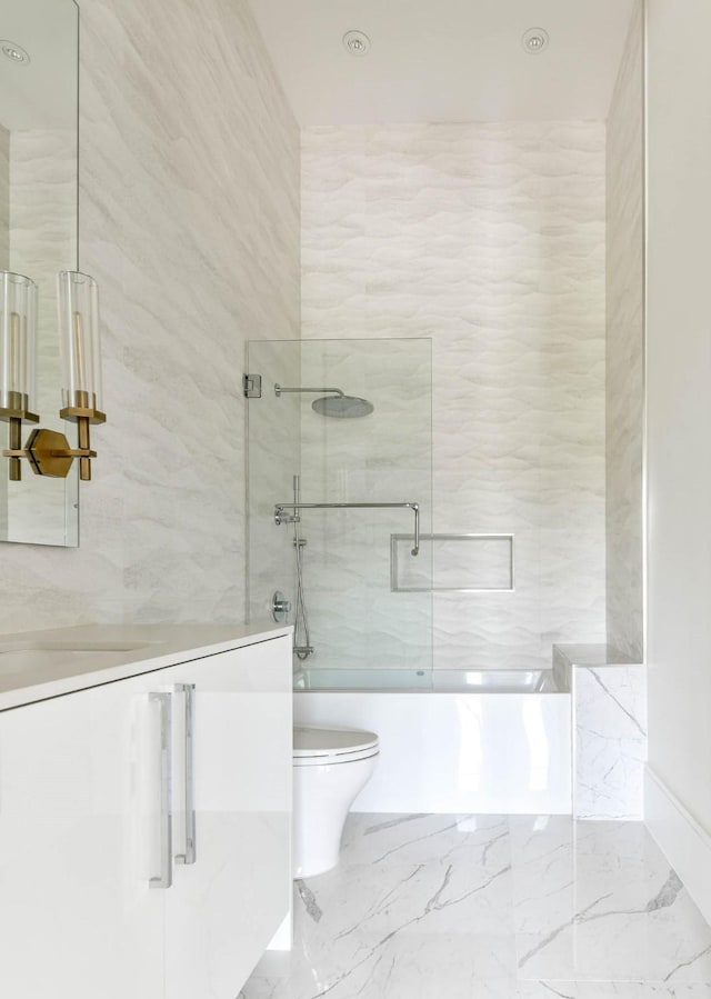 bathroom with marble finish floor, bath / shower combo with glass door, vanity, and toilet