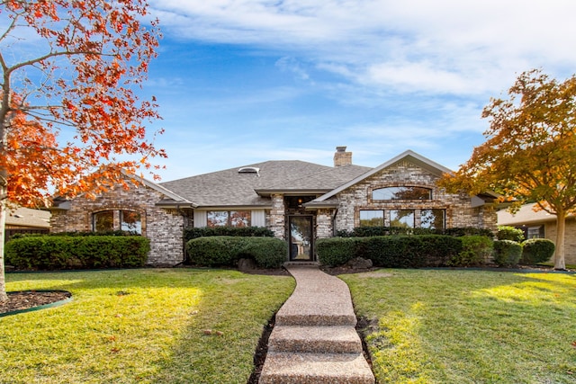 view of front of property with a shingled roof, a chimney, a front yard, and brick siding