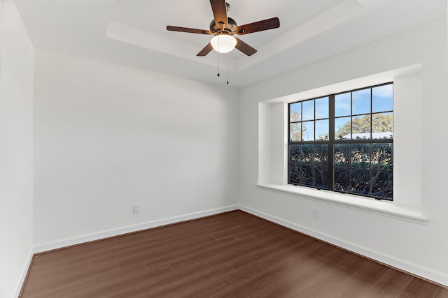 empty room with dark wood-style floors, a tray ceiling, baseboards, and a ceiling fan