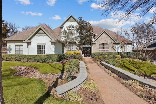 french country home with stone siding, a front lawn, and stucco siding