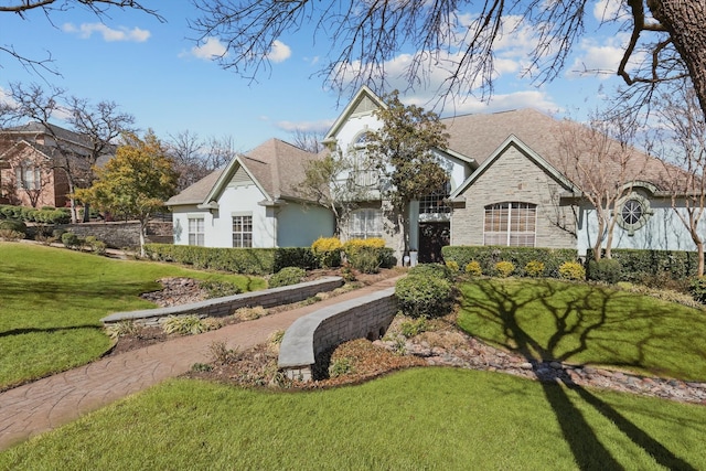 view of front facade with stone siding, roof with shingles, stucco siding, and a front yard