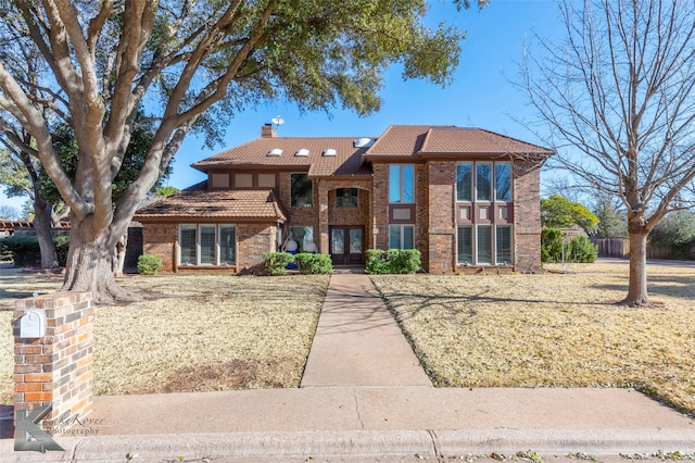 view of front of property featuring french doors, brick siding, a chimney, and a tile roof