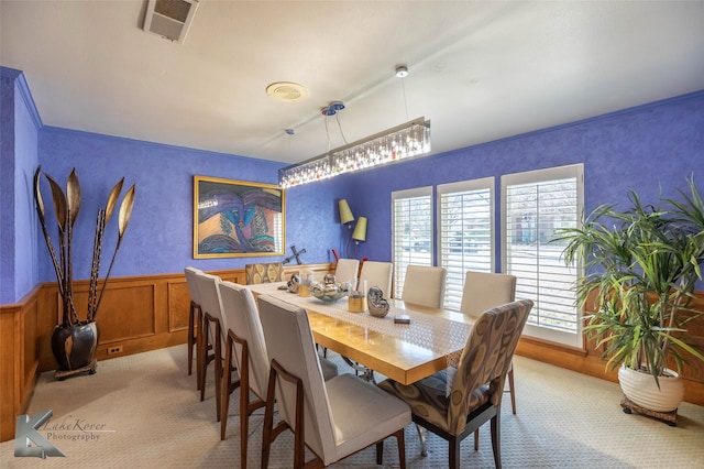 dining space featuring wainscoting, visible vents, crown molding, and light colored carpet