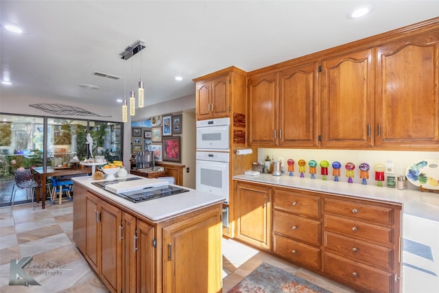 kitchen featuring a center island, light countertops, visible vents, stovetop with downdraft, and brown cabinetry