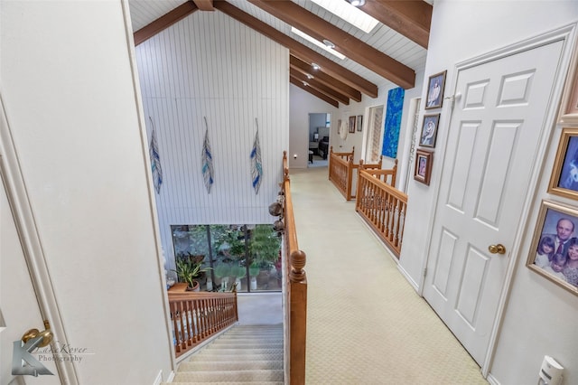 corridor with high vaulted ceiling, a skylight, beam ceiling, and light colored carpet