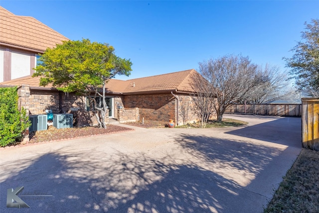 view of property exterior with a tile roof, brick siding, central AC, and fence