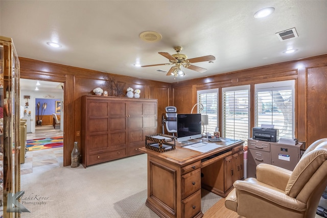 home office featuring wood walls, ceiling fan, visible vents, and light colored carpet