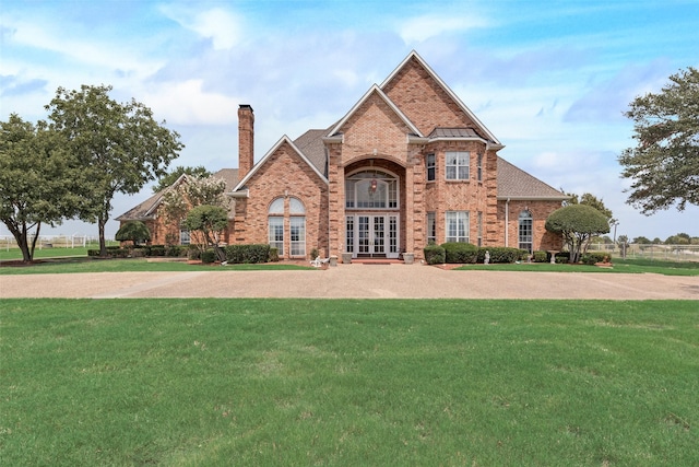 traditional home featuring a front yard, a chimney, french doors, and brick siding