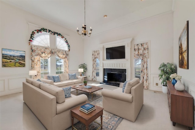 living area featuring a fireplace with raised hearth, a decorative wall, a towering ceiling, wainscoting, and a chandelier