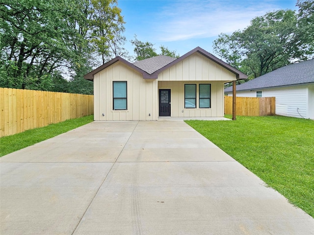 view of front of house featuring roof with shingles, board and batten siding, a front yard, and fence