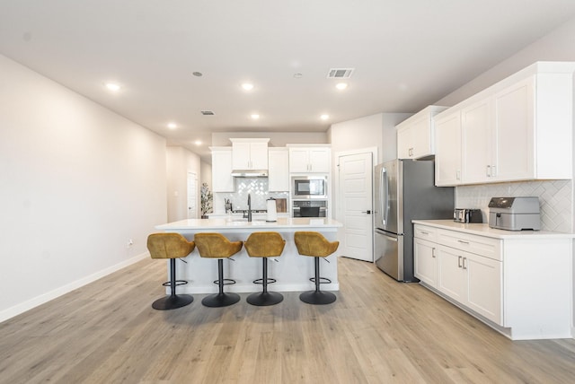 kitchen with a sink, visible vents, light wood-style floors, appliances with stainless steel finishes, and a center island with sink