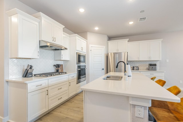 kitchen featuring a breakfast bar area, stainless steel appliances, light countertops, light wood-type flooring, and under cabinet range hood