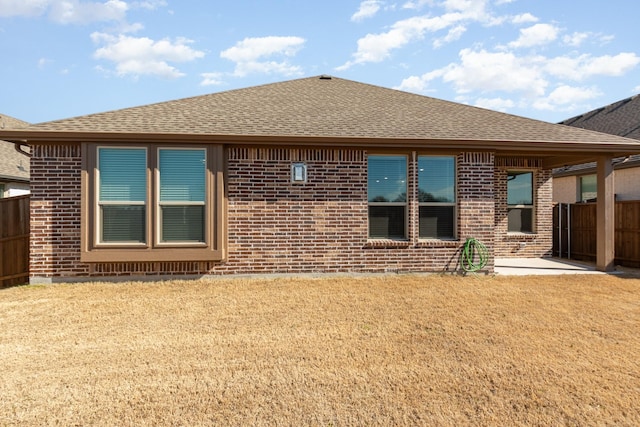 back of property featuring a shingled roof, brick siding, and fence