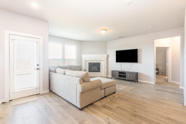 living room with visible vents, a fireplace, light wood-style flooring, and baseboards