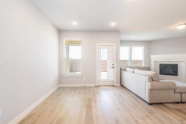 unfurnished living room featuring a high end fireplace, baseboards, and light wood finished floors