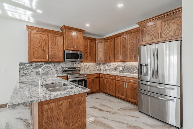 kitchen featuring stainless steel appliances, a peninsula, a sink, marble finish floor, and brown cabinetry