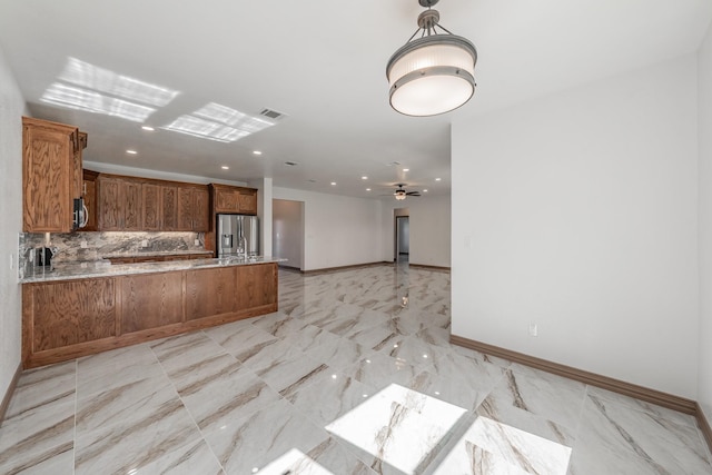 kitchen with stainless steel appliances, backsplash, brown cabinetry, open floor plan, and a peninsula