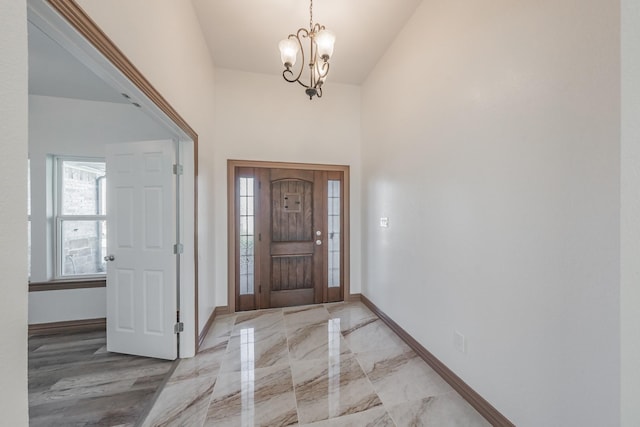 entryway with a towering ceiling, marble finish floor, baseboards, and a chandelier