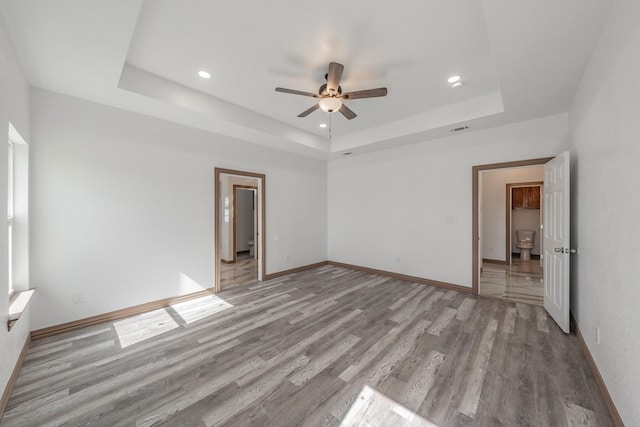 unfurnished bedroom with a tray ceiling, visible vents, light wood-style flooring, and baseboards