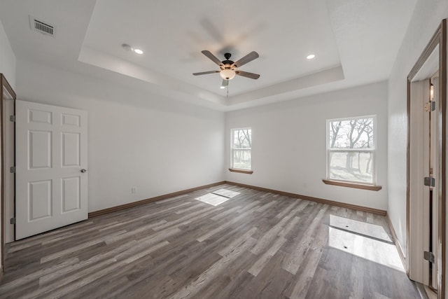 unfurnished bedroom featuring multiple windows, visible vents, a raised ceiling, and wood finished floors